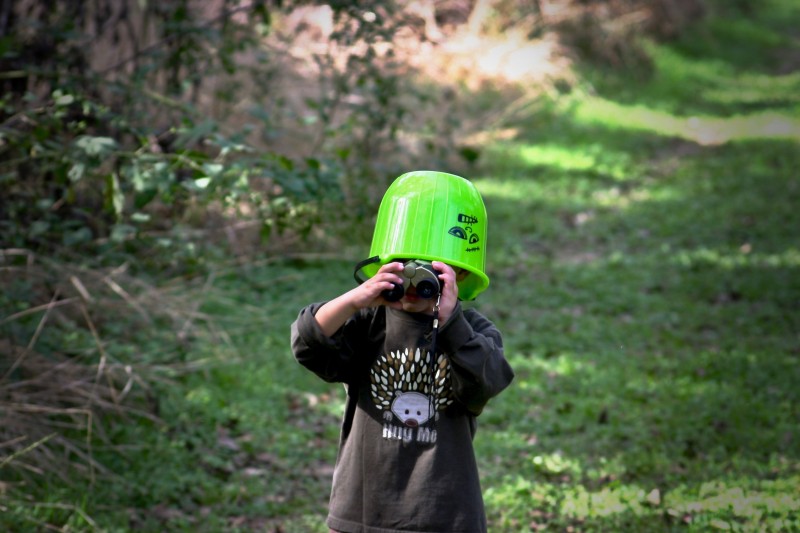 Jongetje met verrekijker en emmer op zijn hoofd gaat op onderzoek uit in de natuur