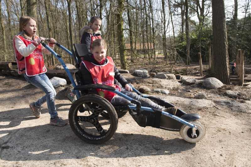 Jongetje in een speciale rolstoel wordt voortgeduwd door het bos